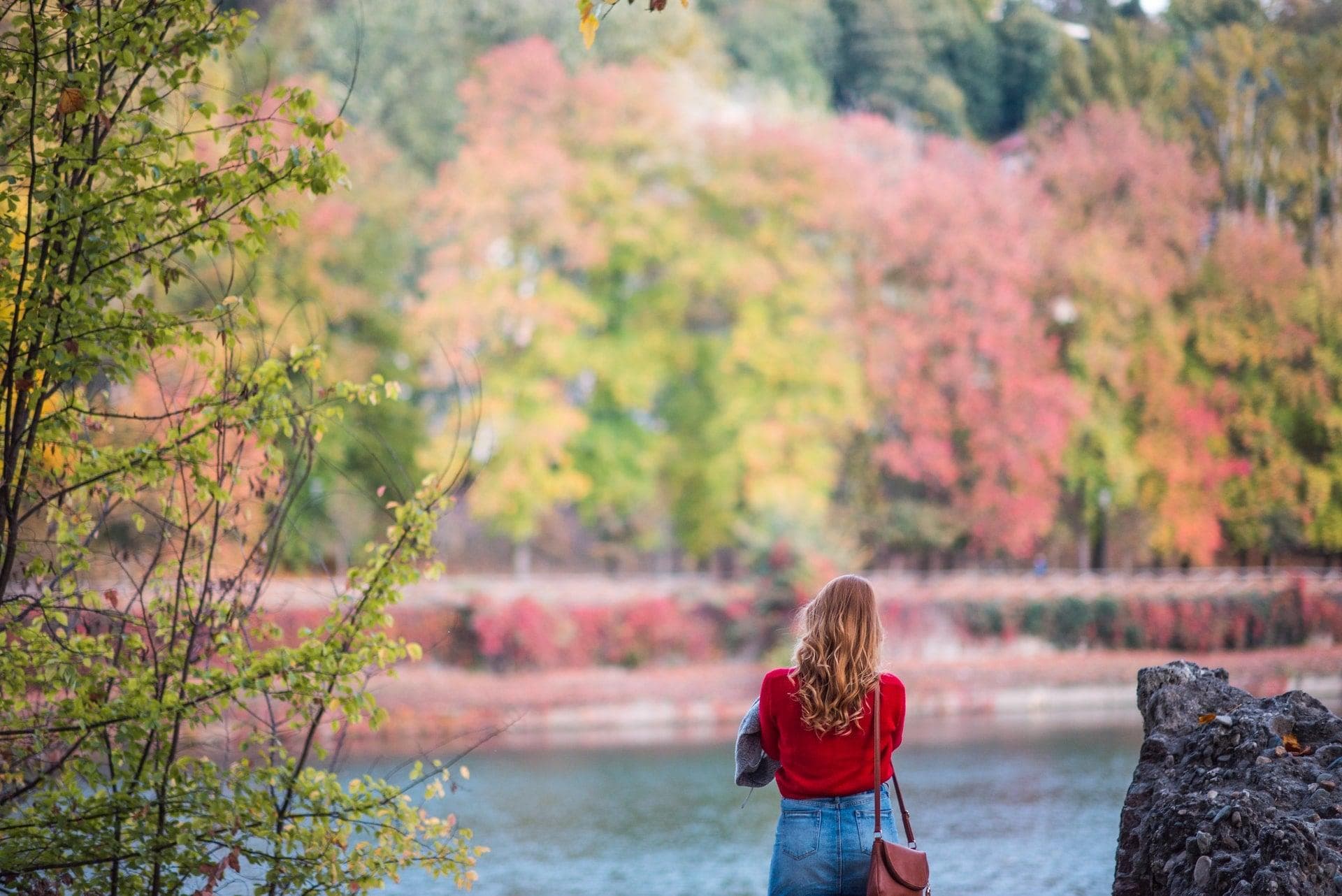 A women dressed in red looking at blossoming trees over a lake.